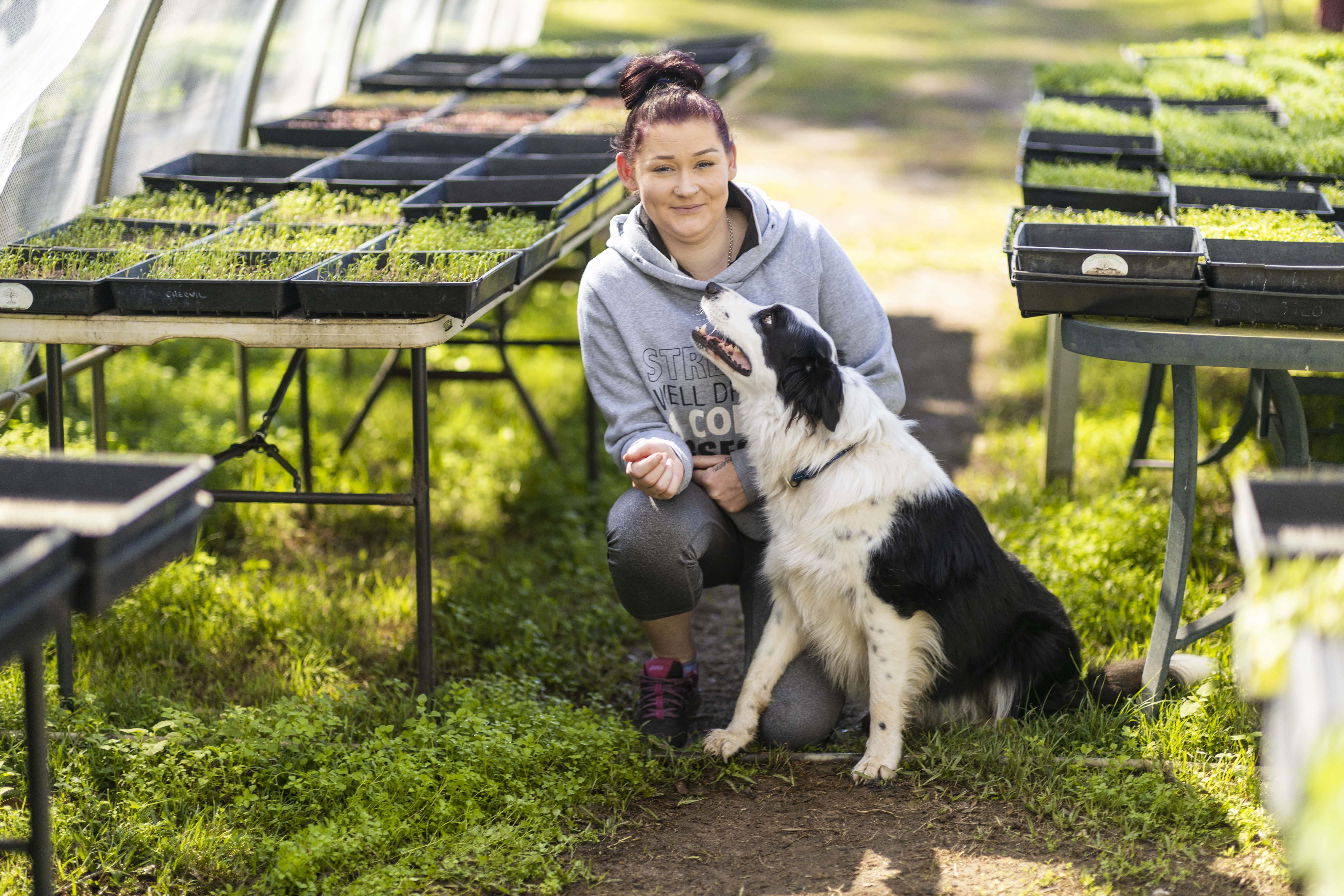 Emma smiles crouching with a dog at the family farm business