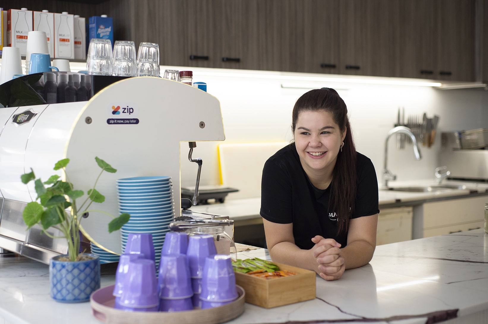 A young woman leans on the counter of a coffee shop