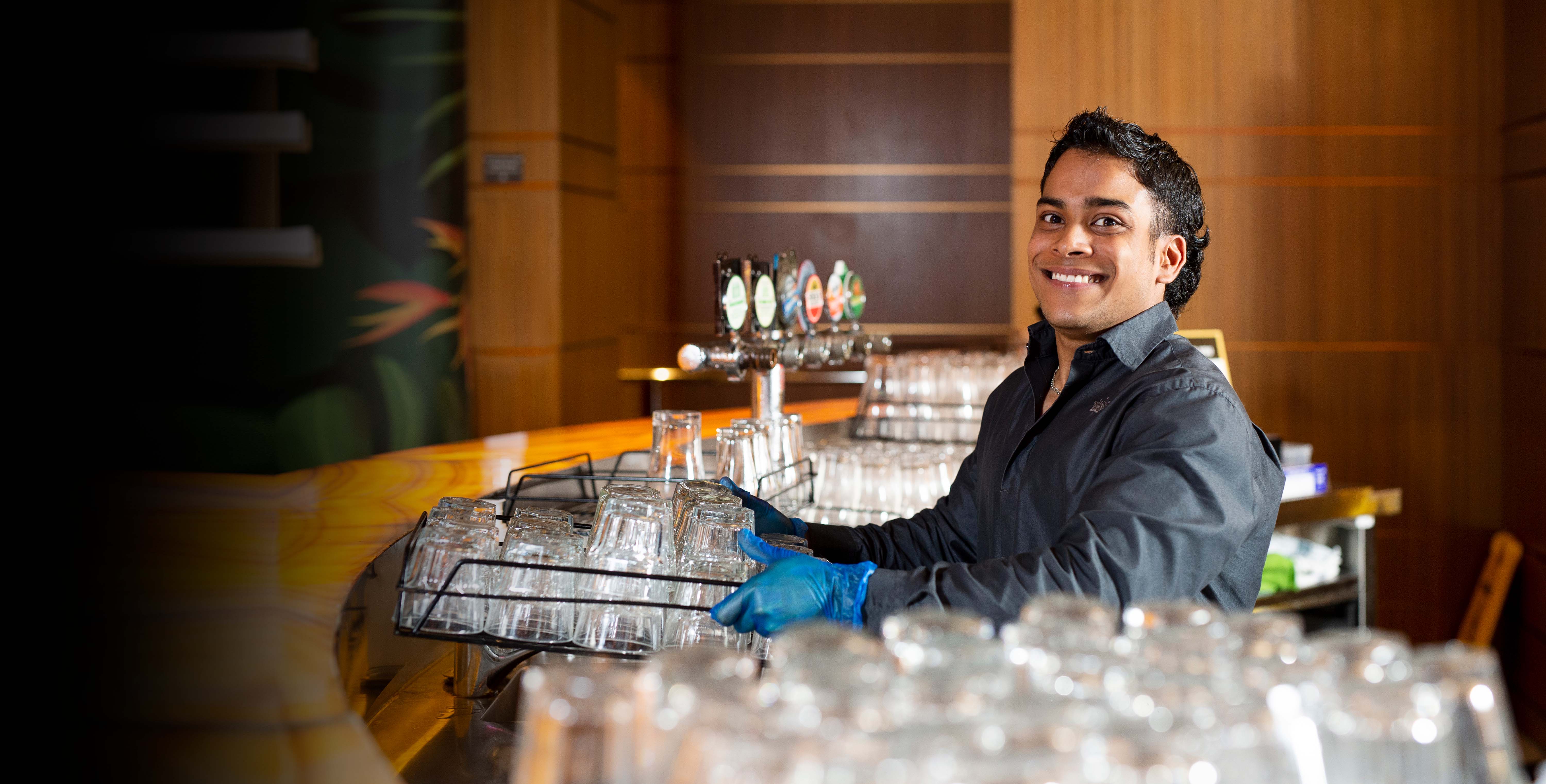 DES participant Clyde smiles holding a tray of glasses