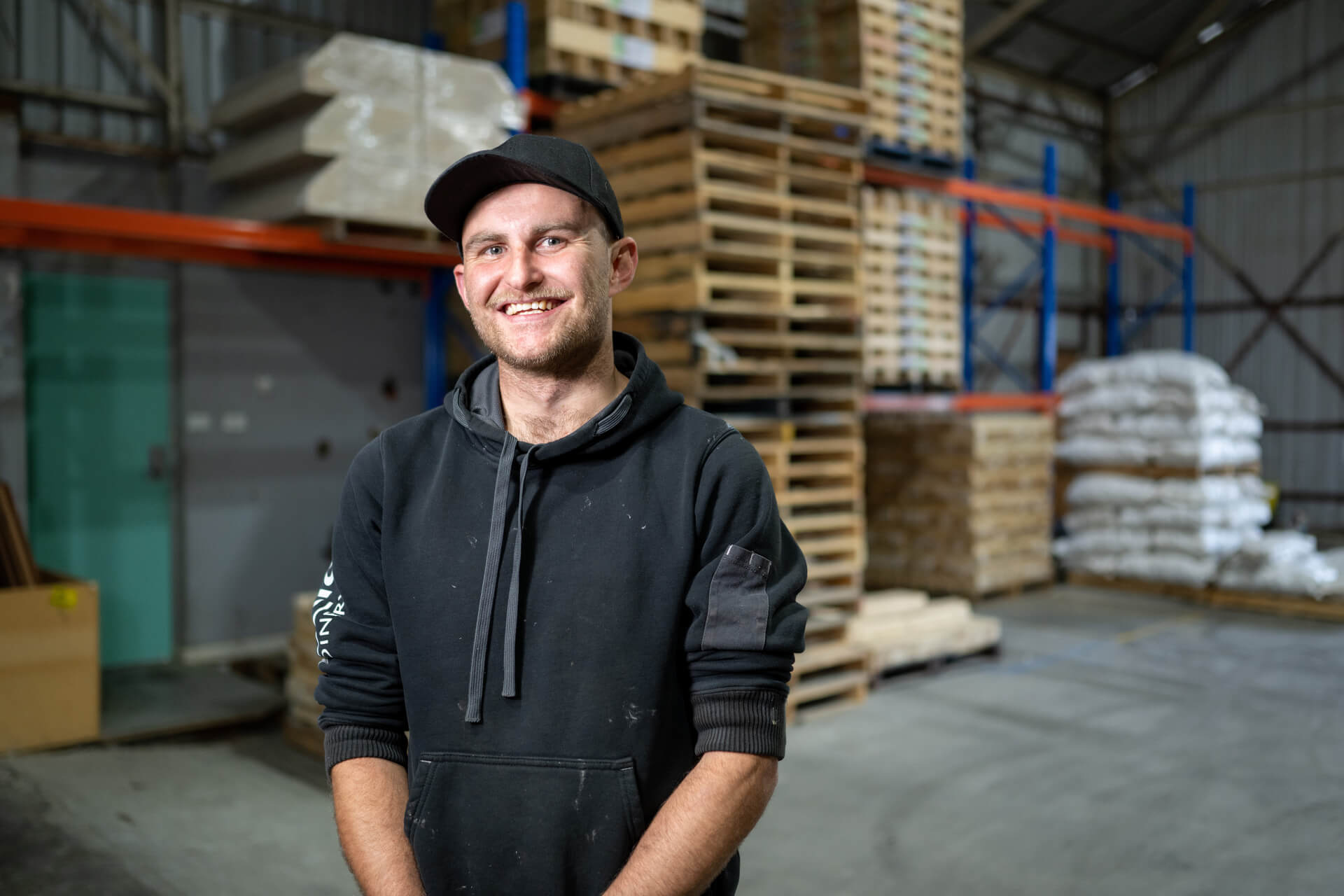 Man in black hooded top smiles while in a warehouse