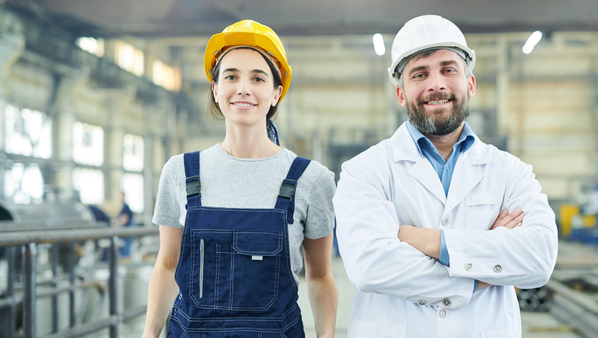 Young female apprentice smiles at camera next to employer in warehouse