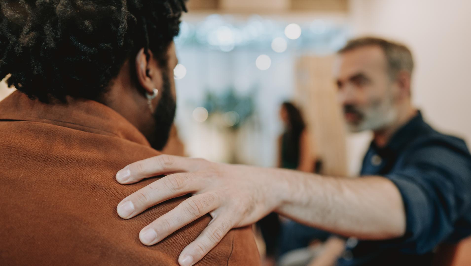 A man puts his hand on another's man shoulder to show support