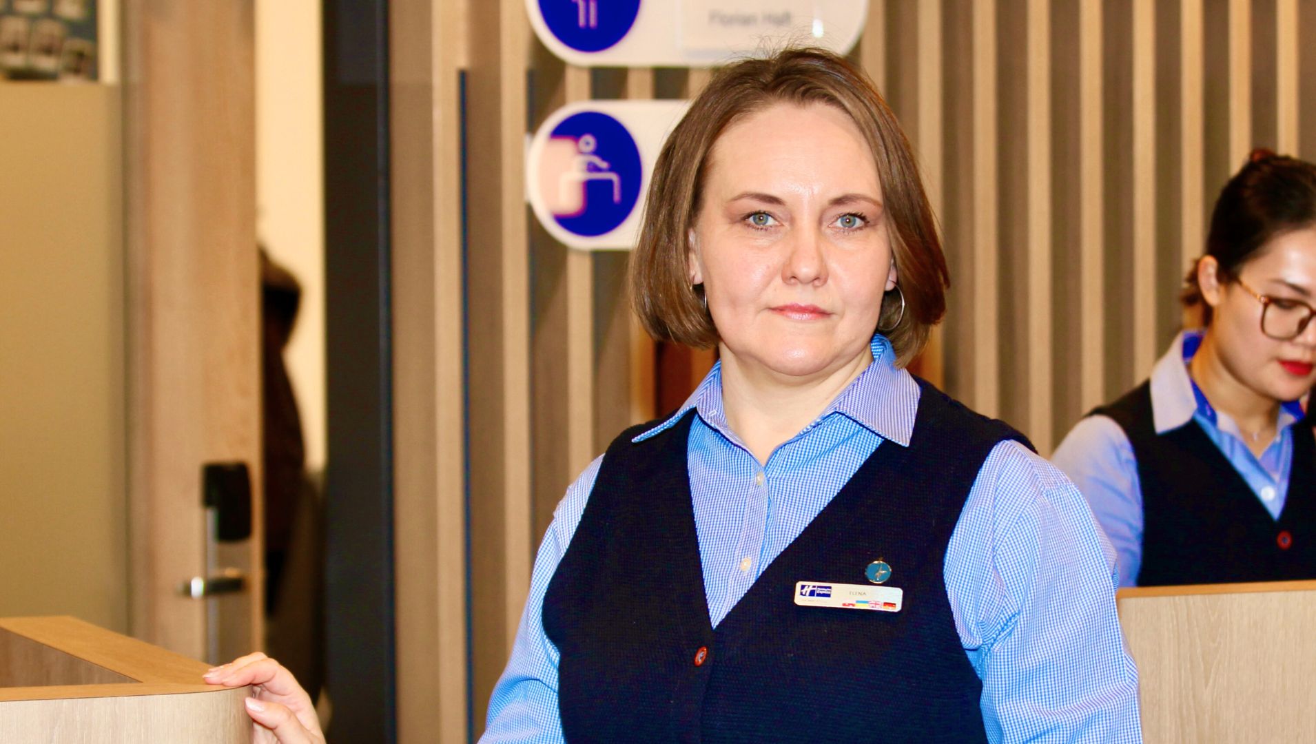 Olena at work wearing hotel staff uniform and standing in the reception