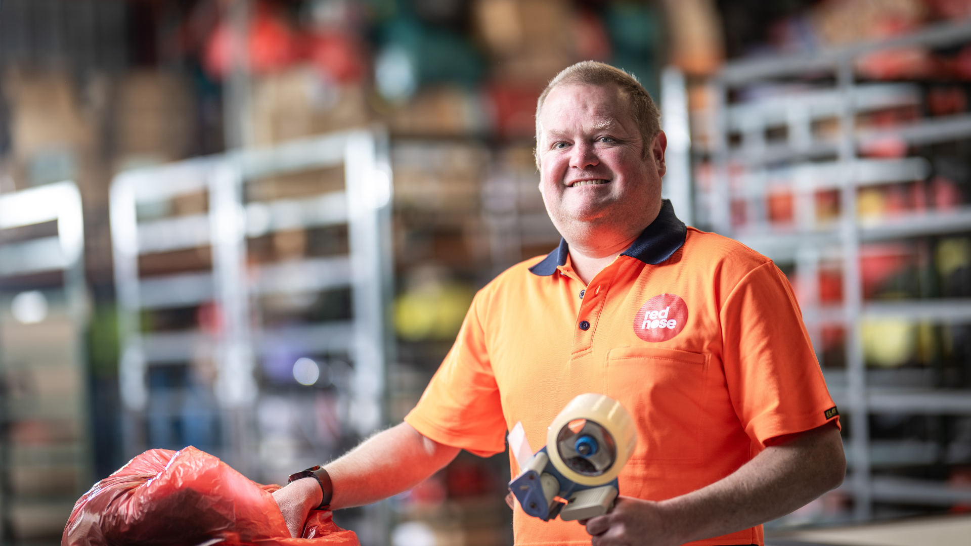 Man smiling leaning on a barrier in a warehouse in an orange top