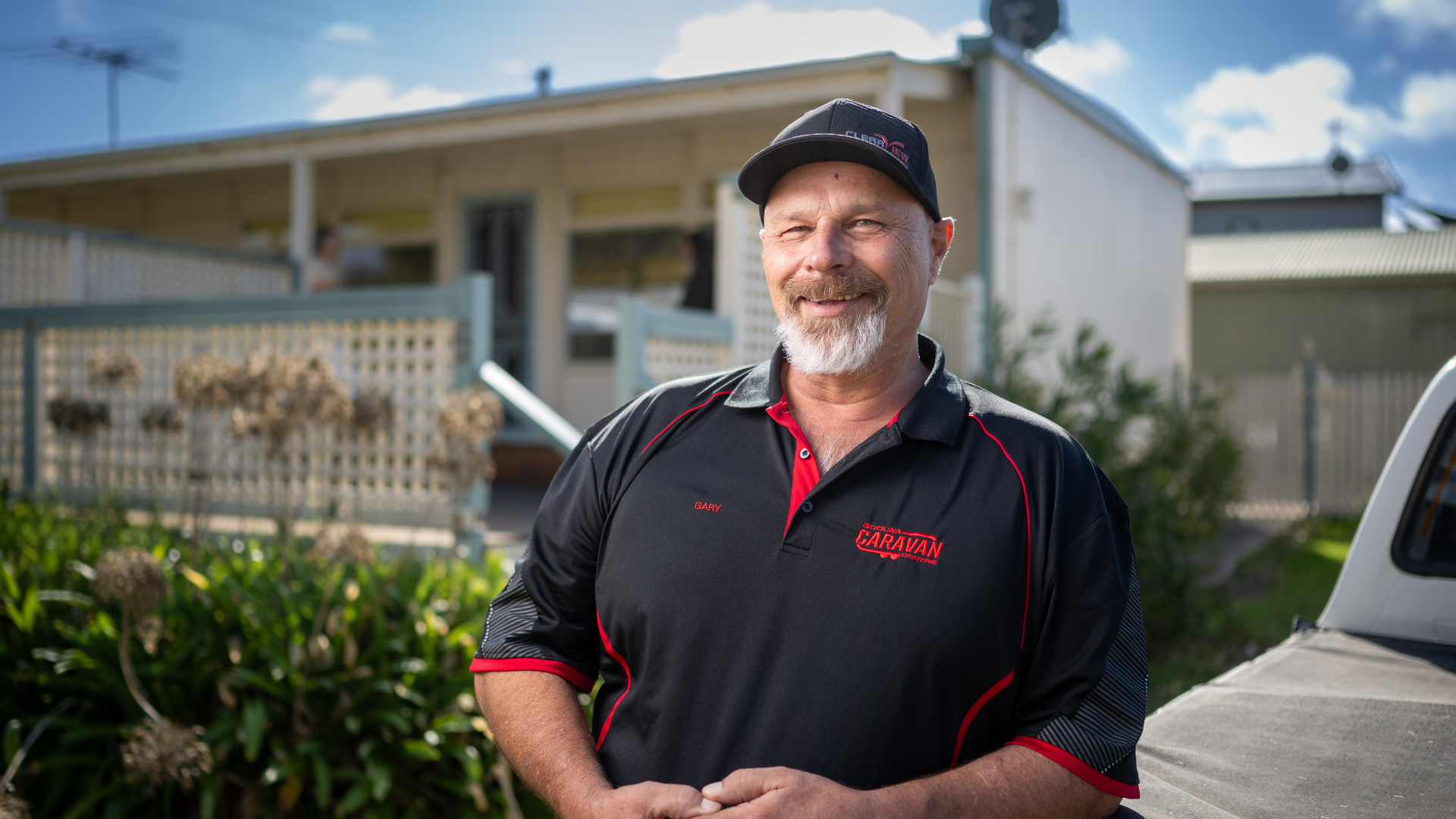 Gary leans against a ute in a black polo and cap