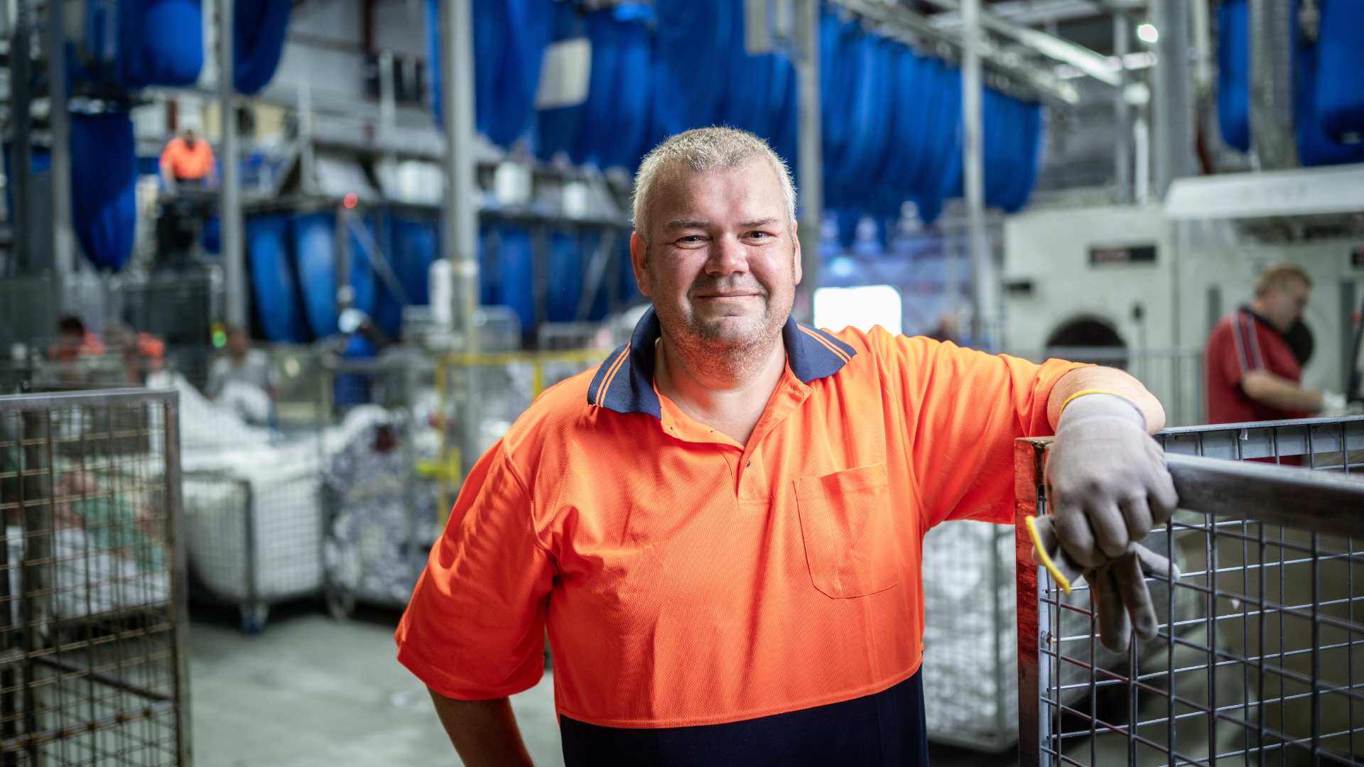 Geoff in an orange tshirt leaning on a machine in a workshop