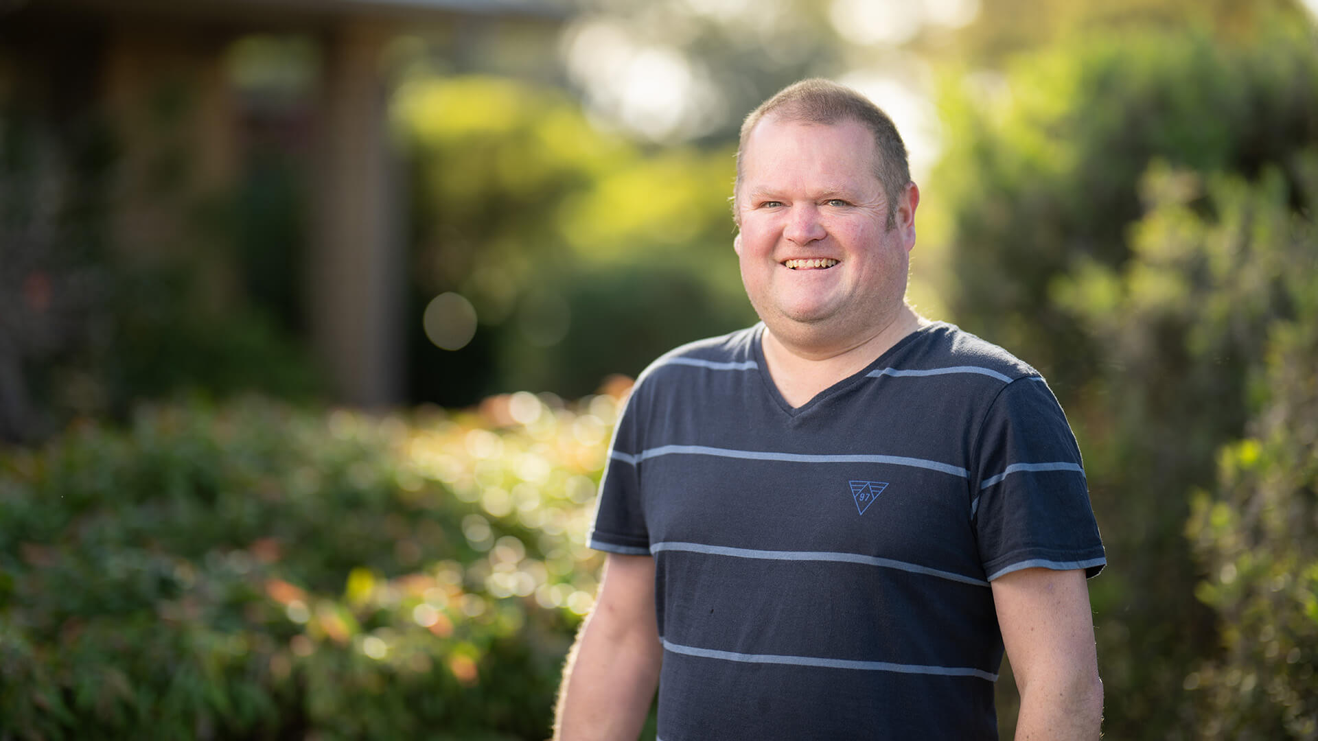 Eric a DES participant with disability smiles outside against a green backdrop