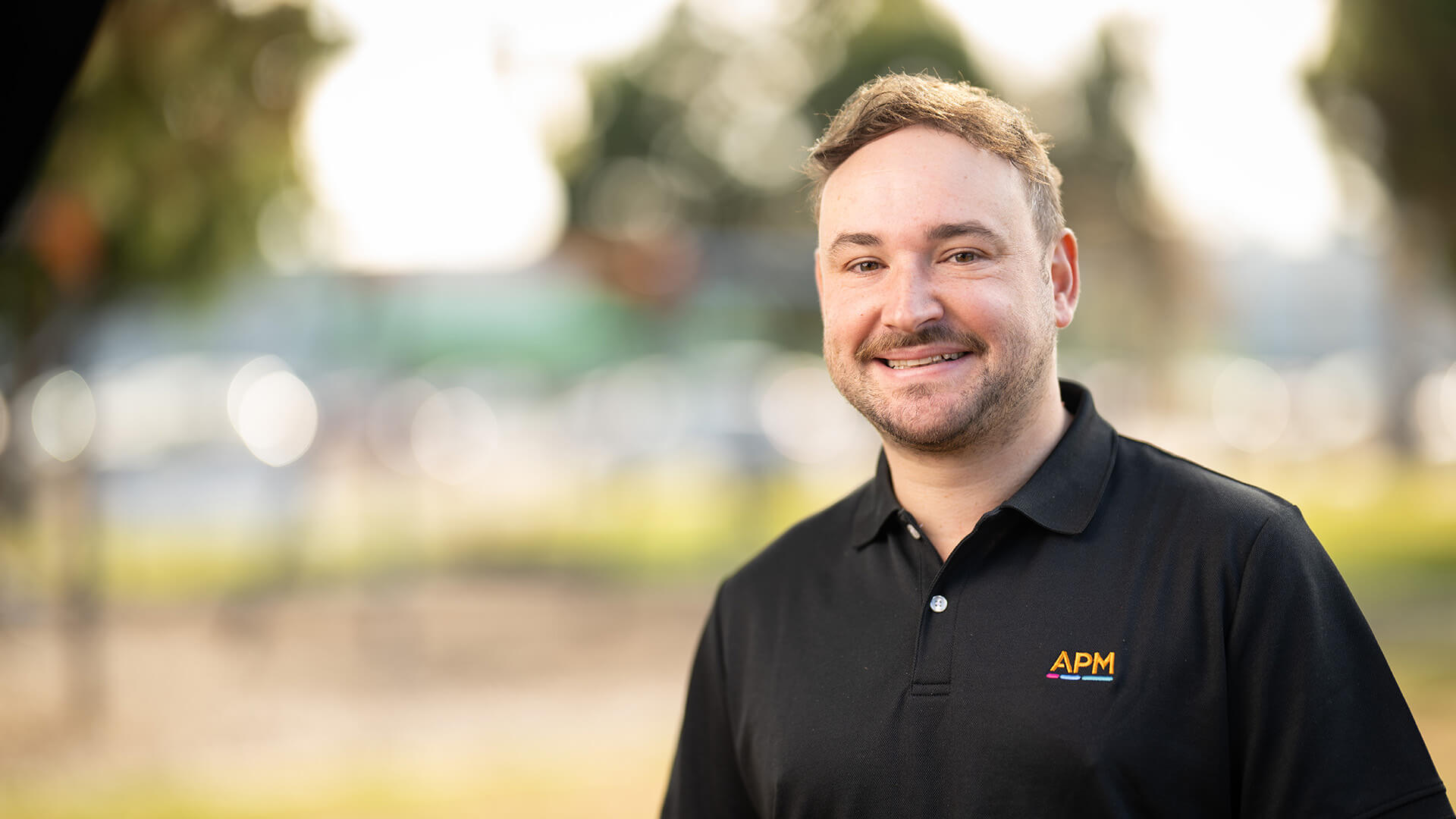 APM Employment Consultant in black polo smiling outside