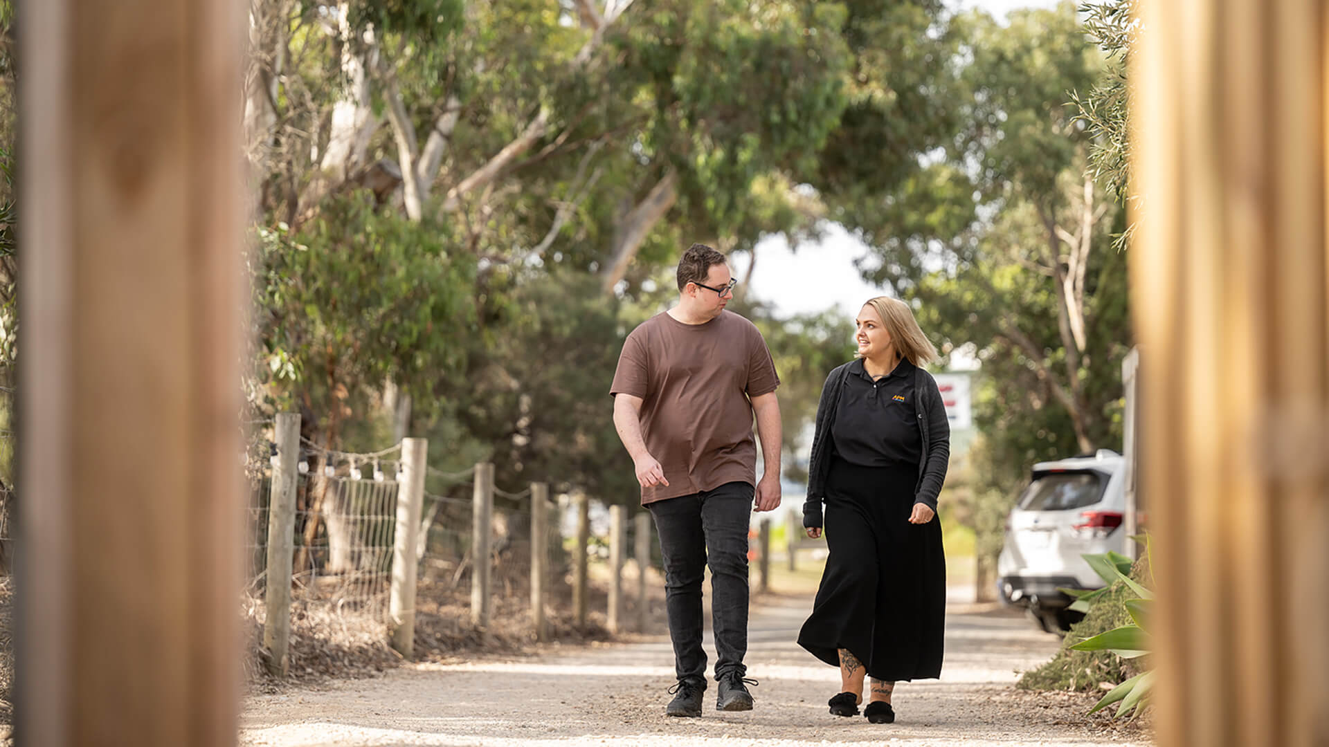 A woman in an APM polo walks alongside a large man in a brown tshirt