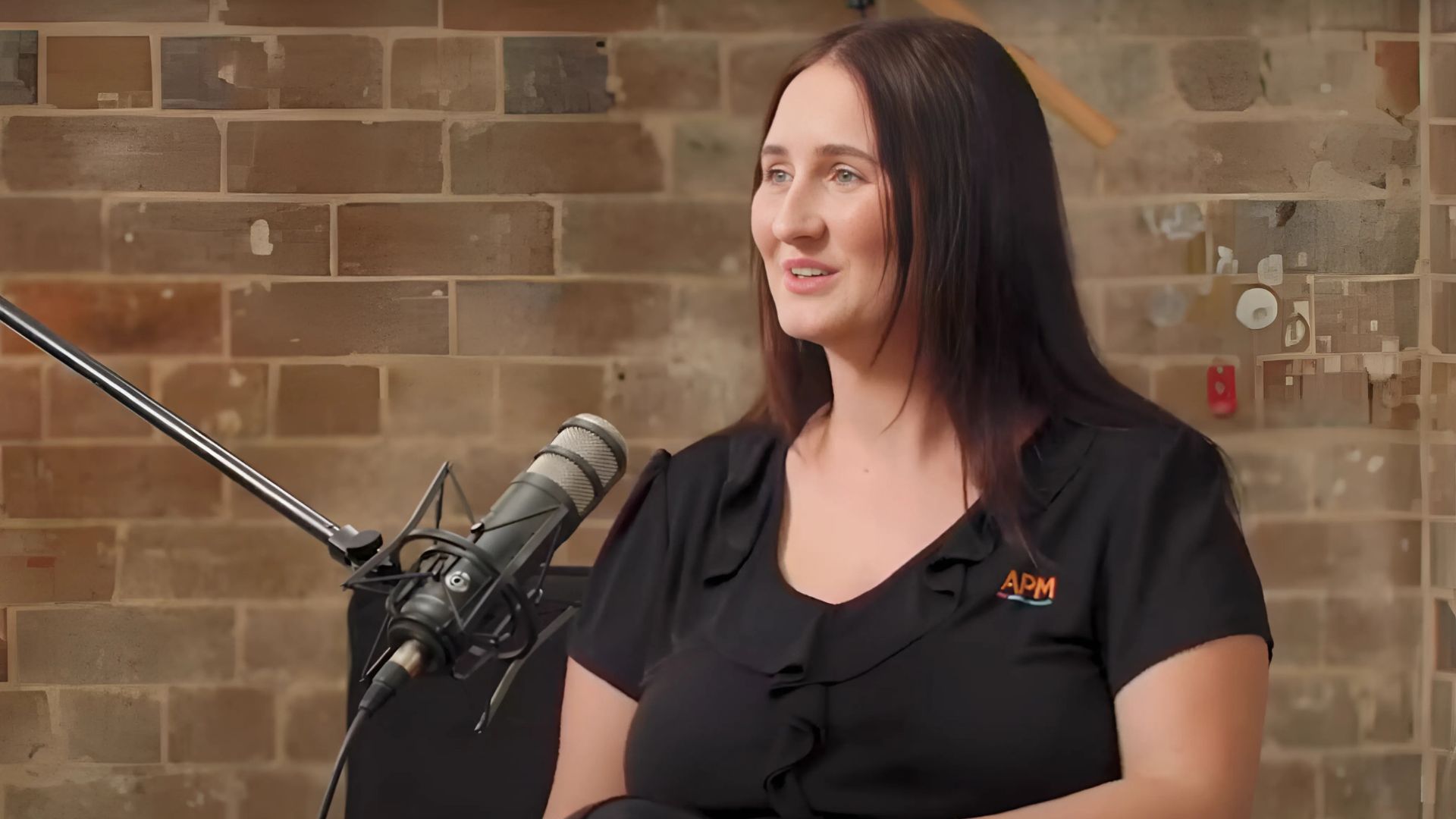 Bree in a black APM top sitting in front of a microphone