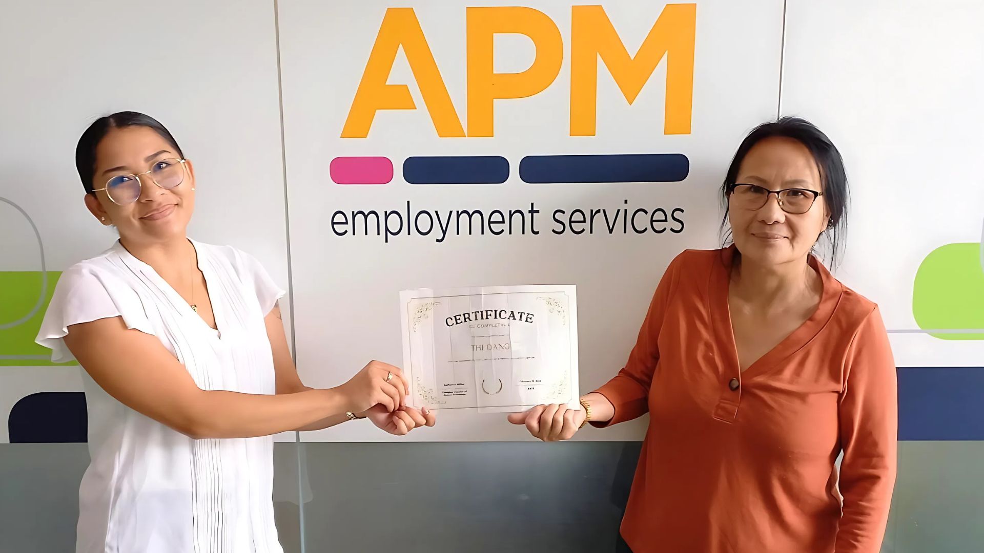 Thi smiling iwitha certificate in front of an APM sign