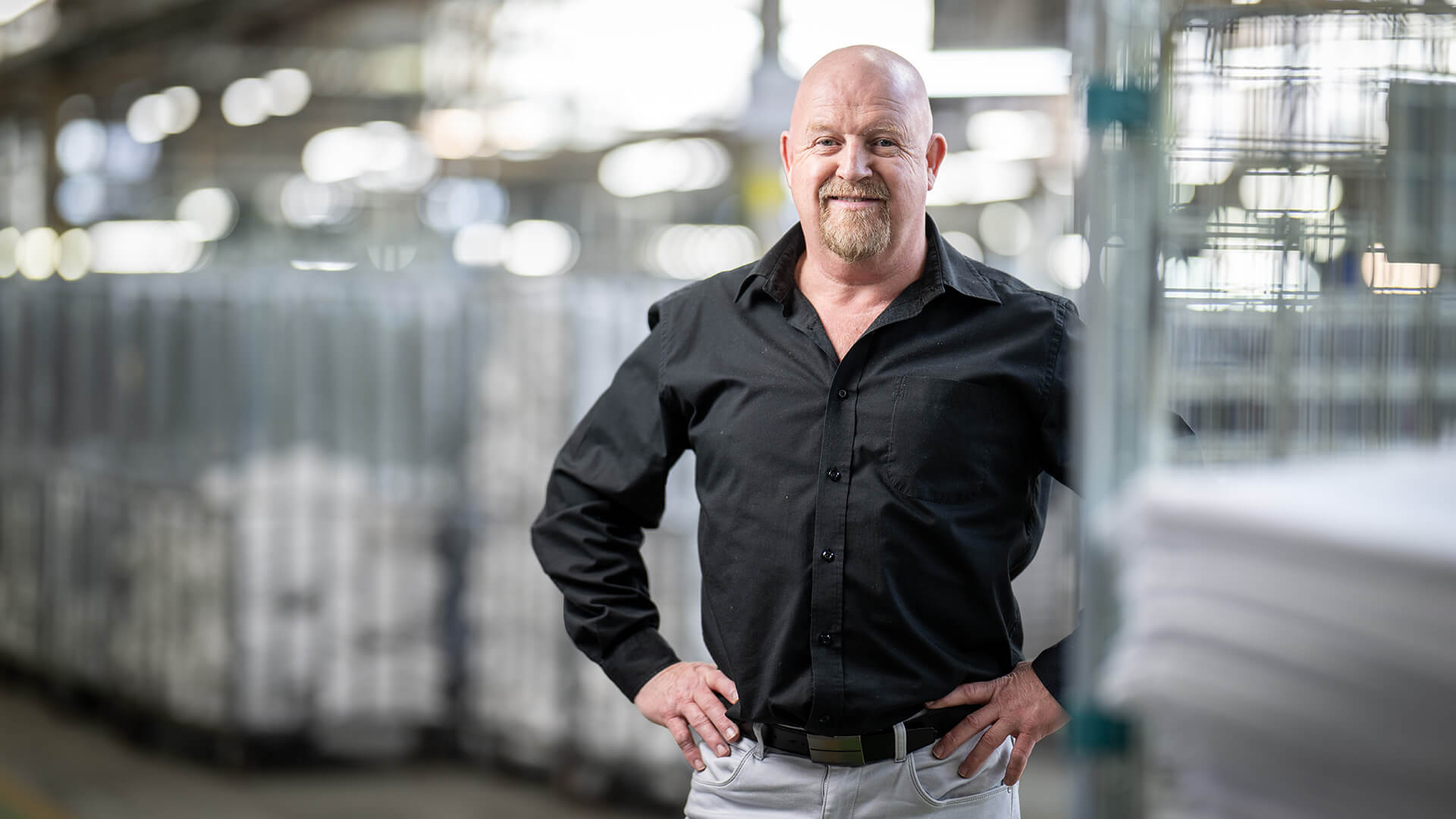 Employer smiles in a black shirt inside a large warehousel