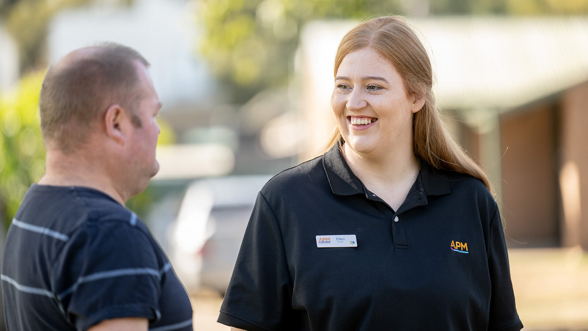 A woman in a black APM polo smiles at a male DES participant