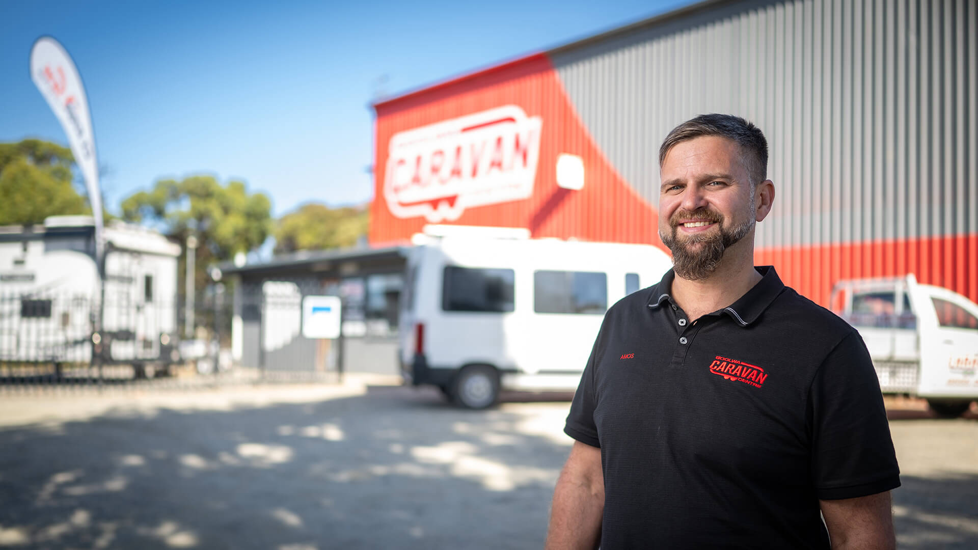 Man smiling in a black polo shirt outside his business