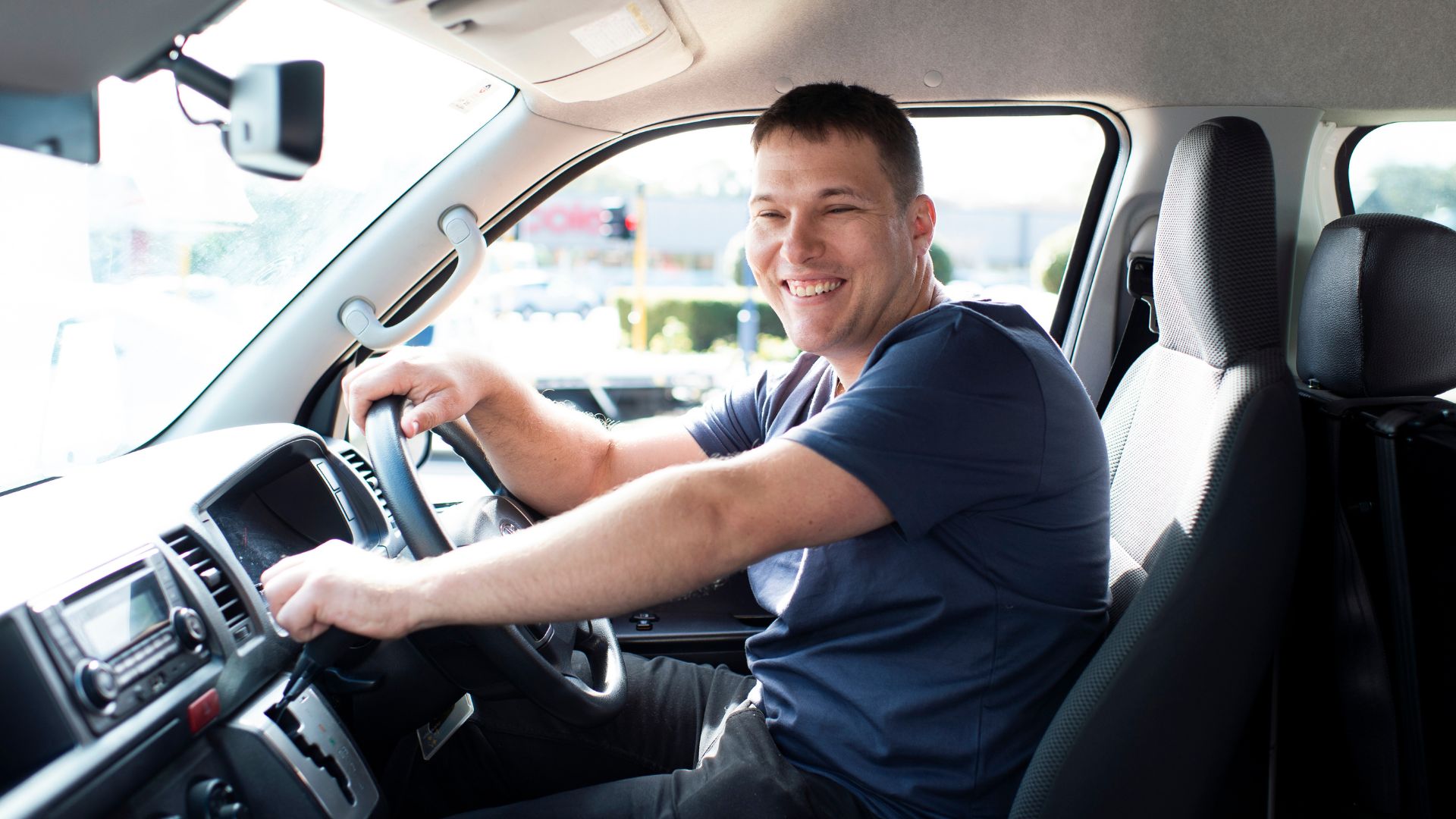 Young man smiles behind the wheel of a work van