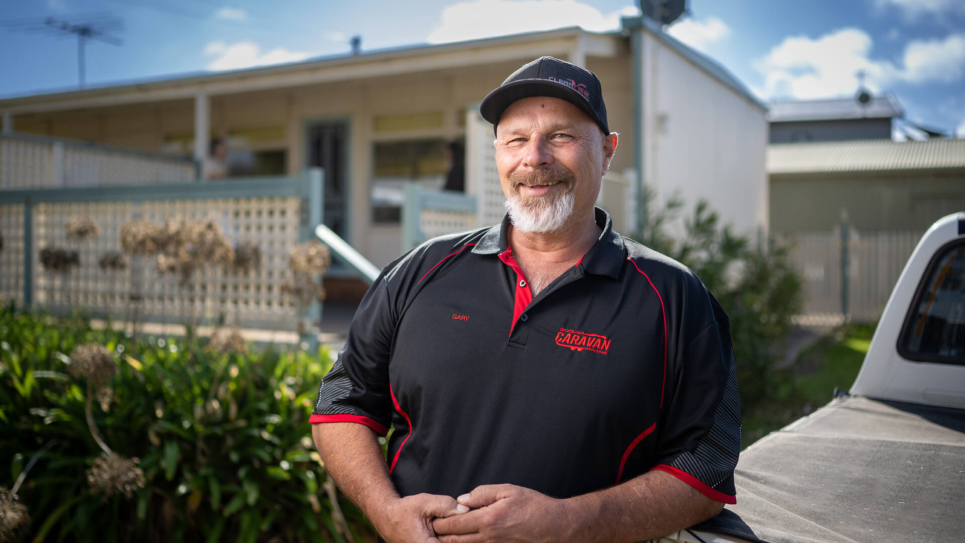 Worker smiles in a black shirt and cap outside a house