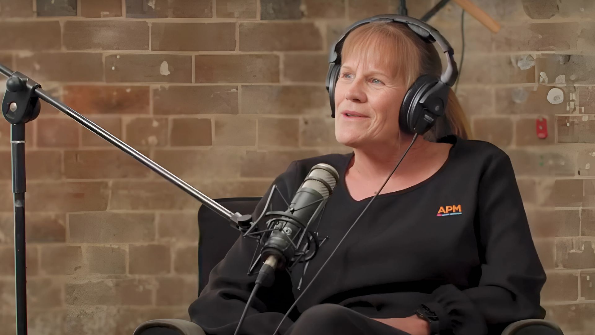 Christine in a black APM top sitting in front of a microphone