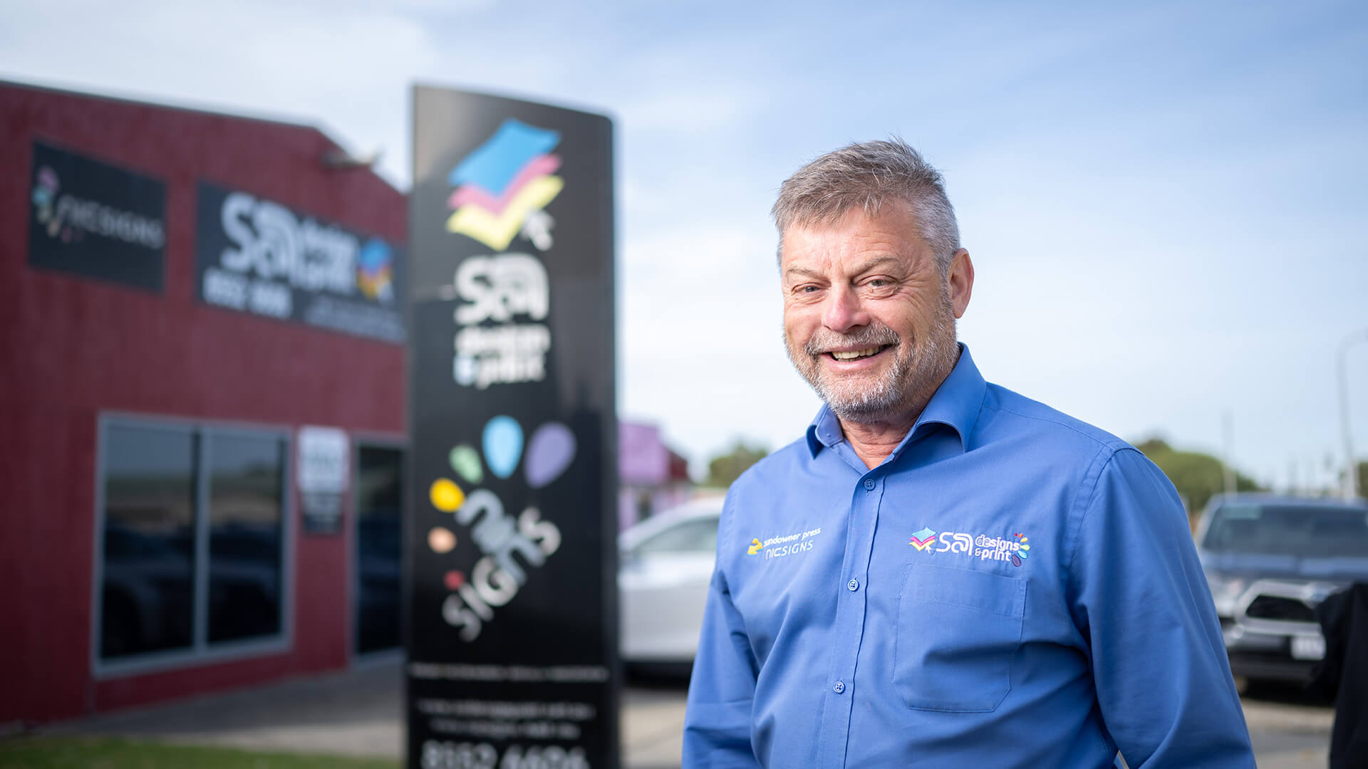 Employer in a blue shirt outside his design business